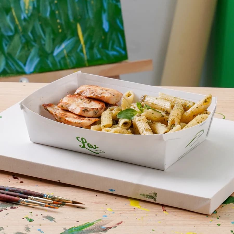 Frango com penne na embalagem da Lev, sobre uma tela com pincéis e respingos de tinta