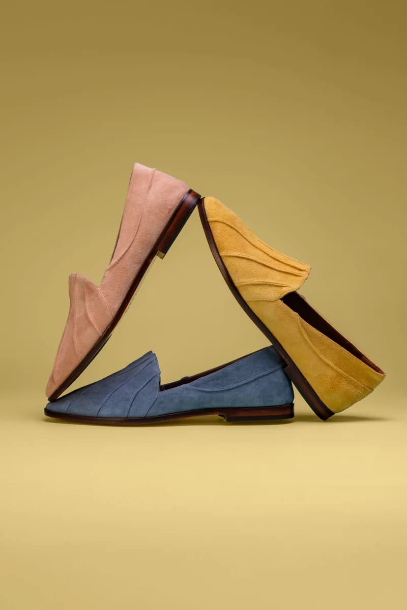 Três mocassins de camurça, rosa, azul e mostarda, apoiados em triângulo sobre fundo ocre